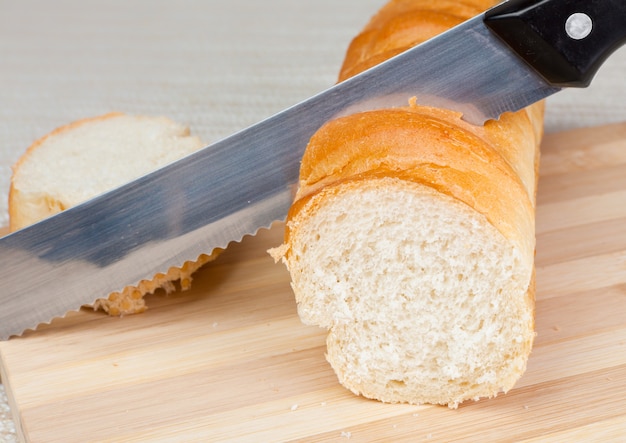 Una pagnotta di pane fatto in casa e una fetta su una tagliere di legno con un coltello da pane.