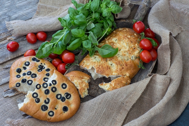 una pagnotta spezzata, focaccia con olive, pomodori e basilico