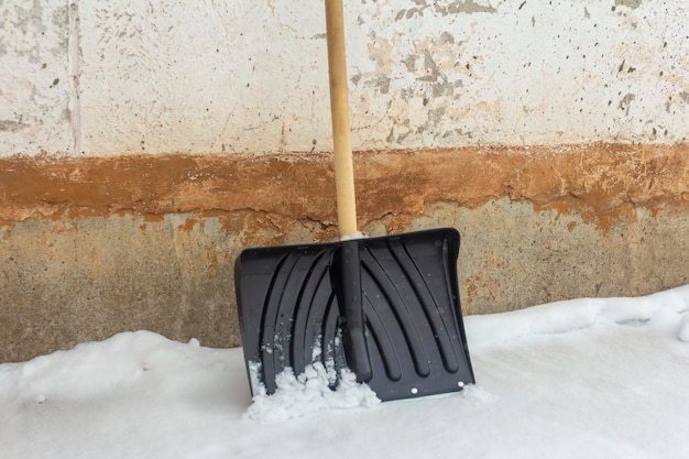 Una pala nera con manico in legno per la rimozione della neve è appoggiata al vecchio muro.