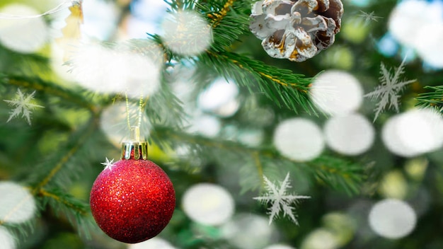 Una palla di Natale rossa è appesa al ramo verde di un albero di Natale con luci bokeh argento. Nuovo Ye