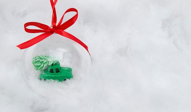 Una palla trasparente con una macchinina e un albero di Natale nella neve