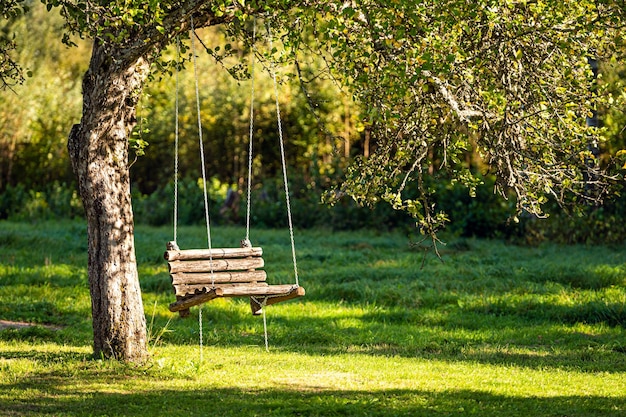 Una panca di legno oscillante appesa a un albero con catene nel giardino di una casa di campagna