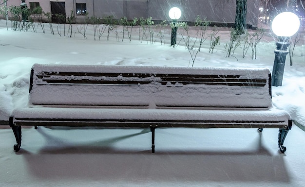 Una panchina sotto la neve in inverno nel parco notturno.