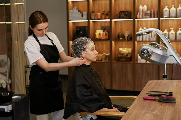 Una parrucchiera fa lo styling dei capelli per la bella giovane donna caucasica in un salone di bellezza