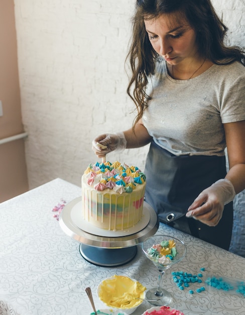 Una pasticcera fa una torta nuziale con le proprie mani e mette addobbi colorati sulle torte alla crema. Preparazione per la celebrazione.