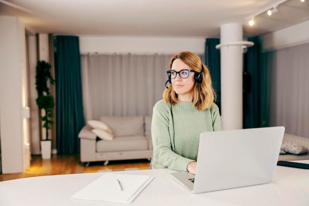 Una pensosa operatrice dell'assistenza clienti che lavora online sul suo laptop nella sua confortevole casa