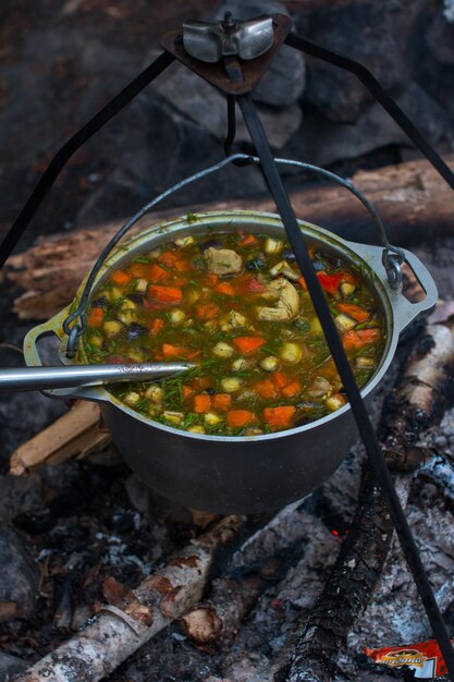 Una pentola da campo pende sul fuoco su un treppiede Cucinare durante un'escursione in campeggio