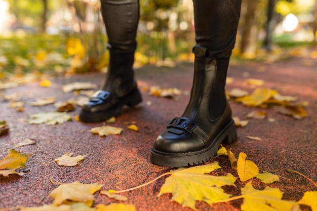 Una persona che indossa stivali neri si trova su un terreno bagnato tra le foglie autunnali.