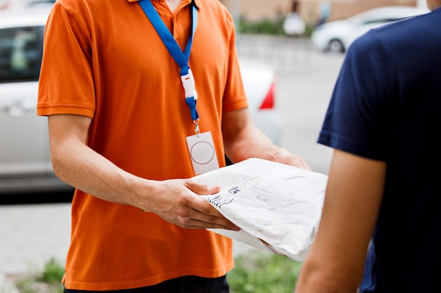 Una persona che indossa una maglietta arancione e un cartellino con il nome sta consegnando un pacco a un cliente. Operaio cordiale, servizio di consegna di alta qualità.