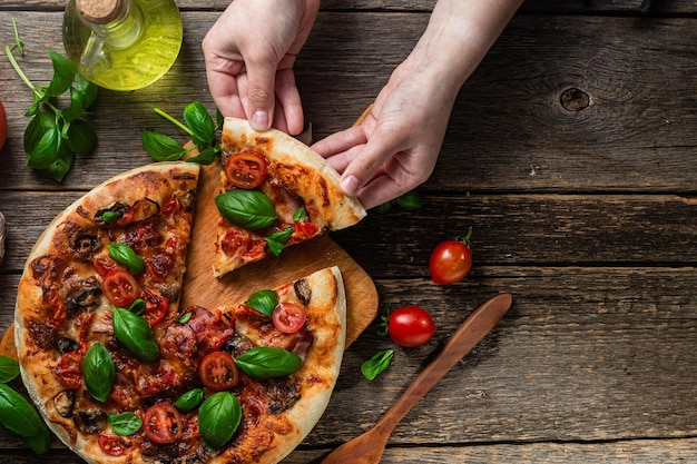 Una persona che prende una fetta di pizza da un tavolo di legno.