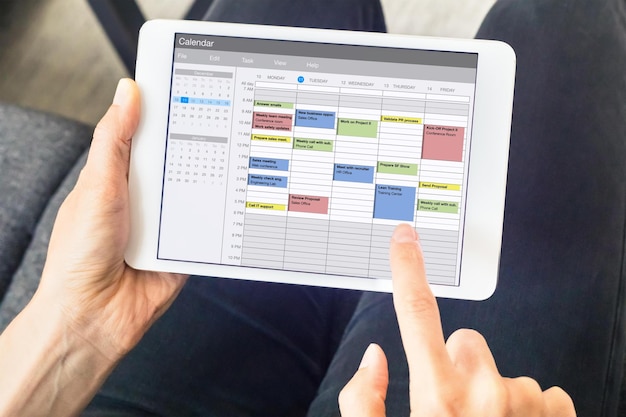 Una persona che utilizza un tablet con un calendario nell'angolo in alto a sinistra e in basso a destra dello schermo.