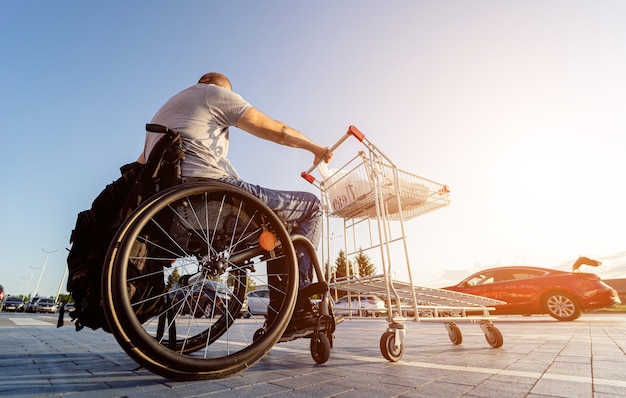 Una persona con disabilità fisica spinge un carrello verso un'auto nel parcheggio di un supermercato