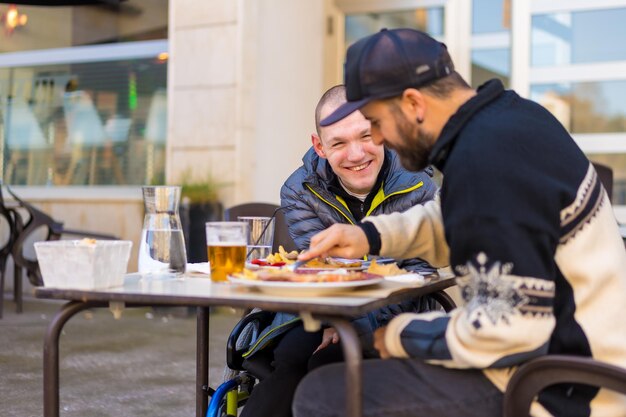 Una persona disabile che mangia e sorride con un amico che si diverte sulla terrazza di un ristorante