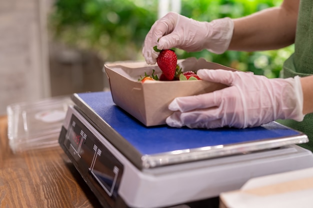 Una persona in guanti che tiene una fragola sopra una scatola su una bilancia