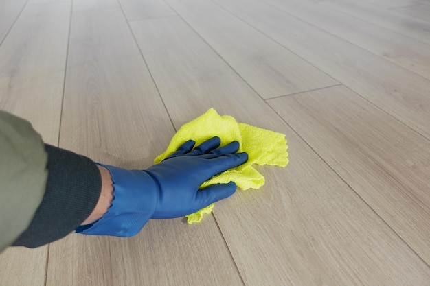 Una persona sta diligentemente pulendo il pavimento usando un panno giallo brillante e indossando guanti blu