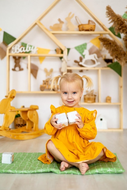 Una piccola bambina oscillante si erge una piramide o una torre di cubi di legno in una casetta e sorride un bambino felice in un vestito giallo