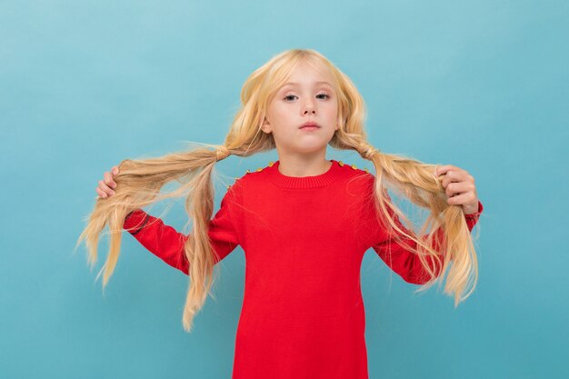 Una piccola bella ragazza con lunghi capelli biondi intrecciati in code isolato su blu