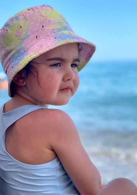 una piccola bella ragazza con un cappello panama e un costume da bagno blu guarda di lato, un bambino piccolo da vicino