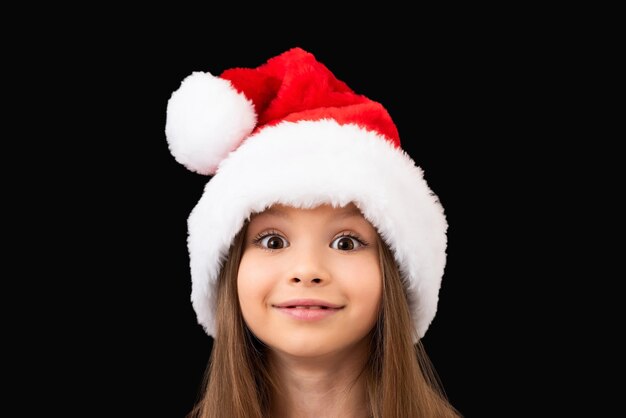 Una piccola bella ragazza in un cappello rosso di Natale pose.