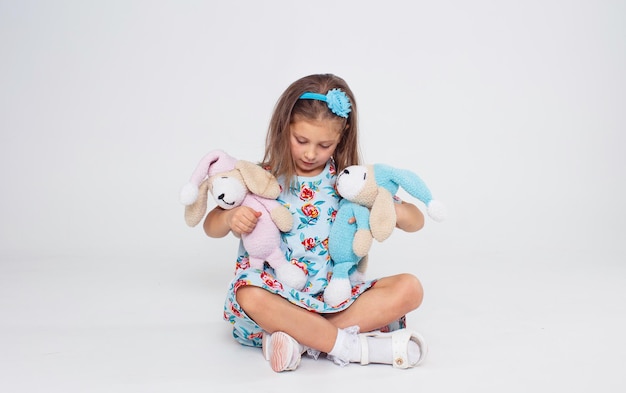 Una piccola bella ragazza in un vestito luminoso abbraccia due giocattoli preferiti su uno sfondo bianco isolato.