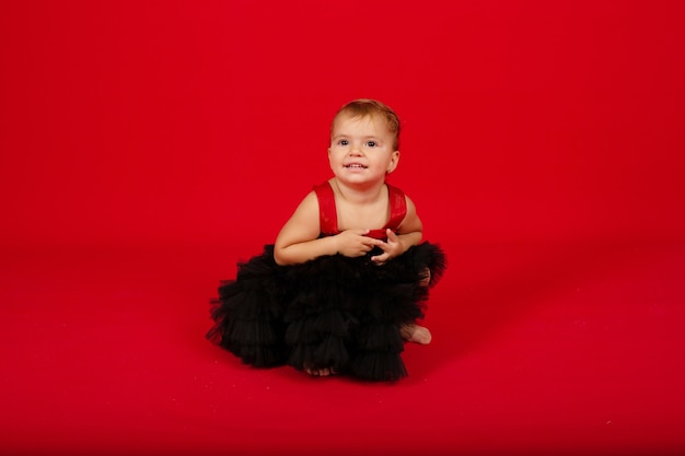 una piccola bella ragazza in un vestito nero è seduta su uno sfondo rosso sorridente