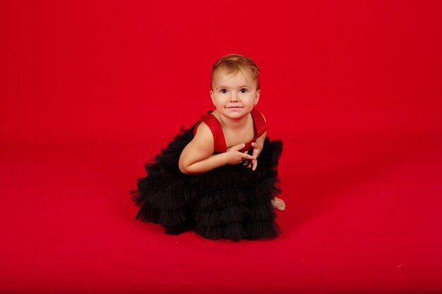una piccola bella ragazza in un vestito nero è seduta su uno sfondo rosso sorridente