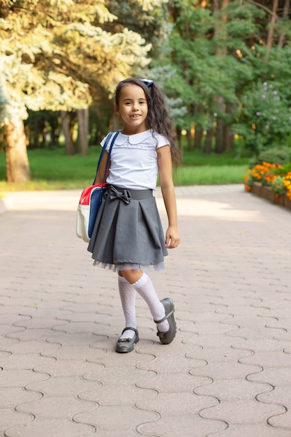 una piccola bella studentessa dai capelli scuri dalla pelle scura in uniforme con una valigetta