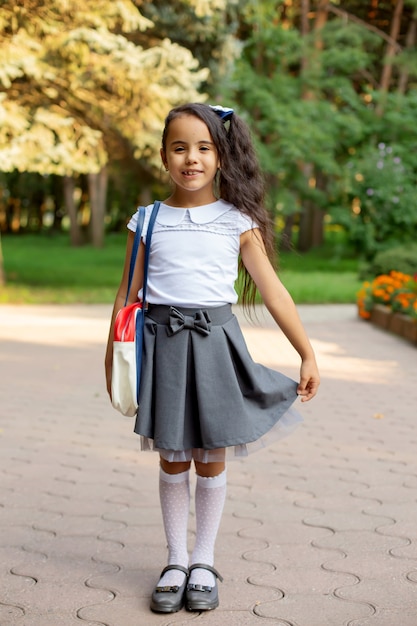 una piccola bella studentessa dai capelli scuri dalla pelle scura in uniforme con una valigetta