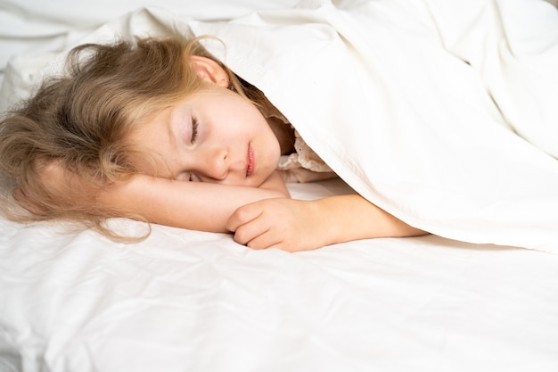 Una piccola bionda sta dormendo dolcemente in un letto con biancheria bianca spazio per il testo sonno sano