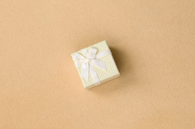 Una piccola confezione regalo in arancione con un piccolo fiocco si trova su una coperta di morbido e felpato tessuto in pile arancione chiaro.