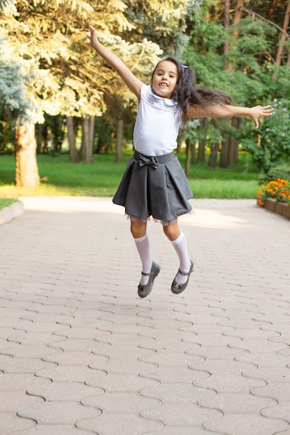 una piccola e bella studentessa dai capelli scuri dalla pelle scura con una camicia bianca uniforme salta