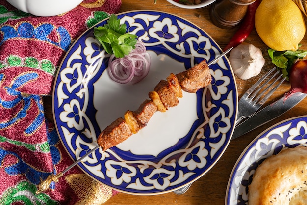 Una piccola porzione di shish kebab di agnello su uno spiedino con cipolla rossa e prezzemolo in una piastra con un modello nazionale uzbeko
