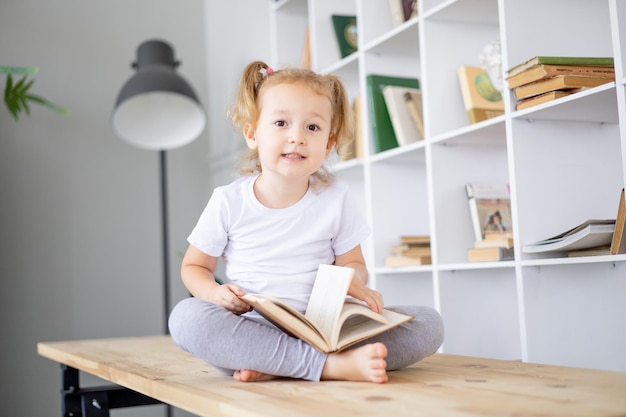 Una piccola ragazza bionda legge libri in una biblioteca luminosa a casa istruzione e scienza per bambini