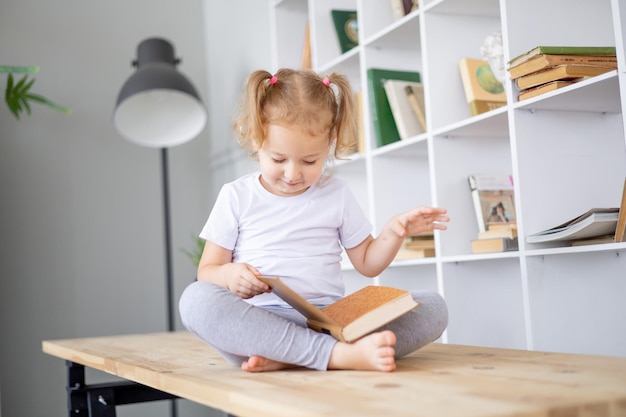 Una piccola ragazza bionda legge libri in una biblioteca luminosa a casa istruzione e scienza per bambini