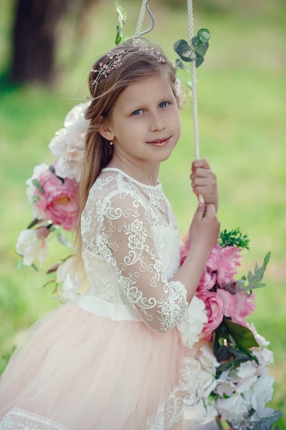 Una piccola ragazza europea bionda in un bel vestito posa vicino al paesaggio nel campo. Baldacchino, fiori, tenerezza, ghirlanda,