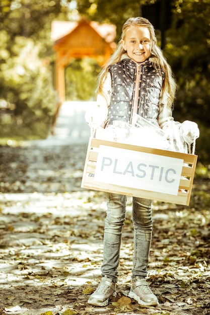 Una piccola ragazza sorridente che tiene una scatola di plastica in una buona giornata