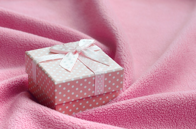 Una piccola scatola regalo in rosa con un piccolo fiocco si trova su una coperta