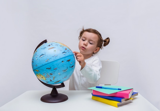 Una piccola studentessa si siede con un globo a un tavolo su uno sfondo bianco isolato