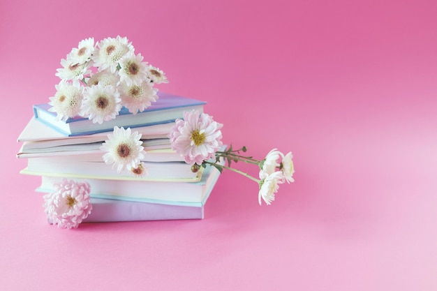 Una pila di libri con segnalibri di fiori di crisantemo freschi, su sfondo rosa