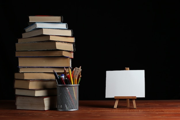 Una pila di libri su un tavolo, un piccolo cavalletto con una carta bianca bianca o un foglio di carta