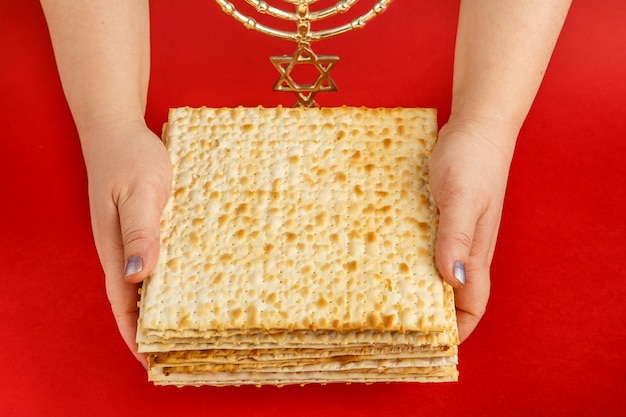 Una pila di matzo in mani femminili su una superficie rossa vicino alla menorah