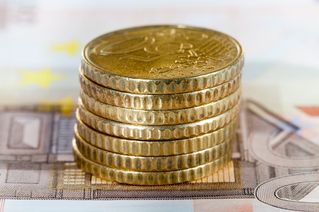 Una pila di monete europee da cinquanta euro, adagiata su una banconota da dieci euro, un primo piano di contanti