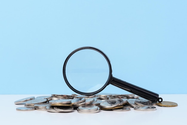Una pila di monete metalliche e una lente di ingrandimento in plastica su sfondo blu Il concetto di aumentare le sovvenzioni fiscali