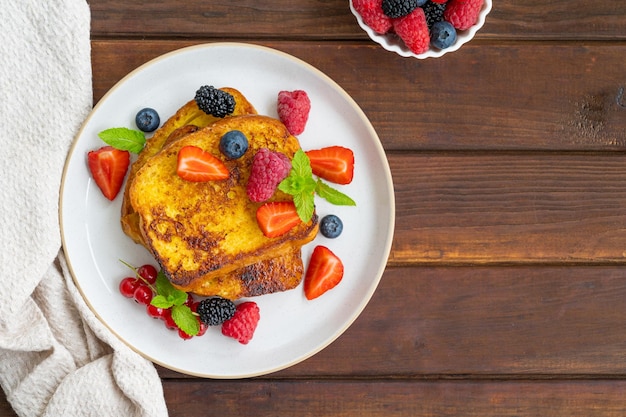 Una pila di pane tostato francese su un piatto con frutti di bosco freschi petali di mandorle e miele Deliziosa colazione