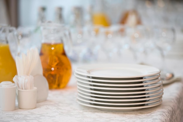 Una pila di piatti bianchi sul tavolo con una caraffa di bicchieri di plastica per il succo