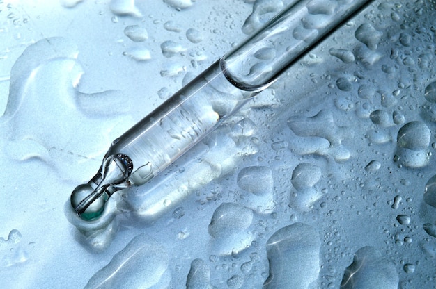 Una pipetta cosmetica con liquido giace su un bicchiere bagnato. avvicinamento.