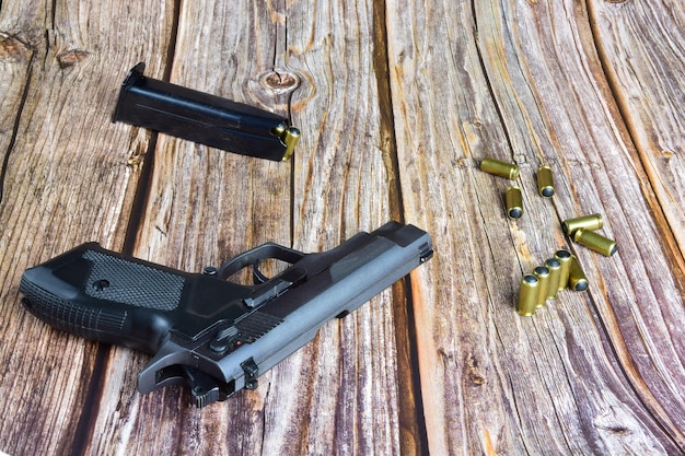 Una pistola nera e diverse cartucce traumatiche giacciono su vecchie tavole di legno marrone.