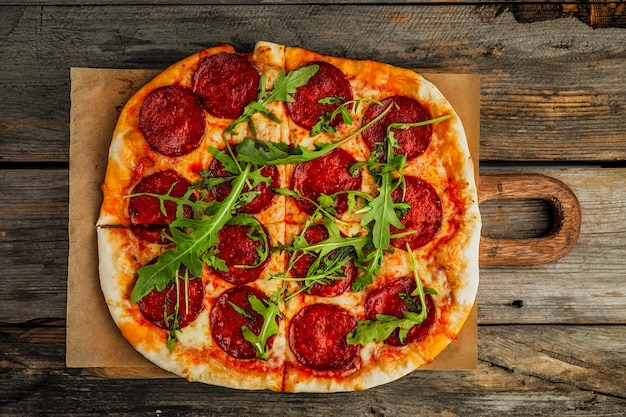 Una pizza ai peperoni con insalata di rucola su una tavola di legno