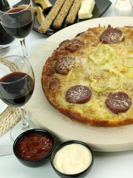 Una pizza con sopra delle salsicce accanto a due bicchieri di vino.
