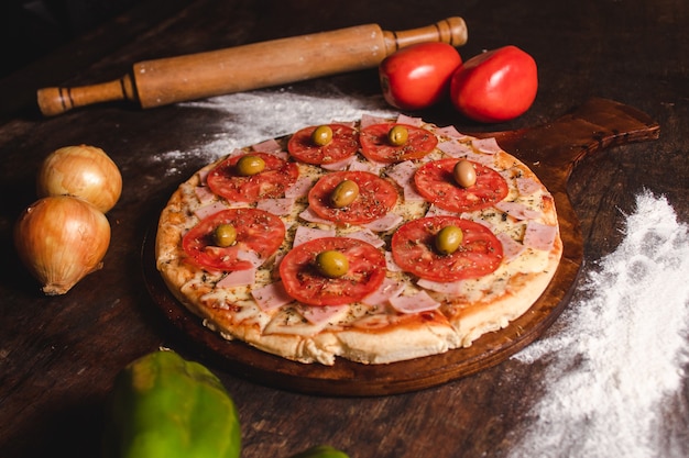 Una pizza con tanto formaggio, pomodoro, origano e olive su un tavolo di legno.